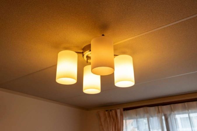 Plafonnier à quatre abat-jours cylindriques en verre côtelé diffusant une lumière chaude dorée, une option classique pour choisir ses luminaires d'intérieur.