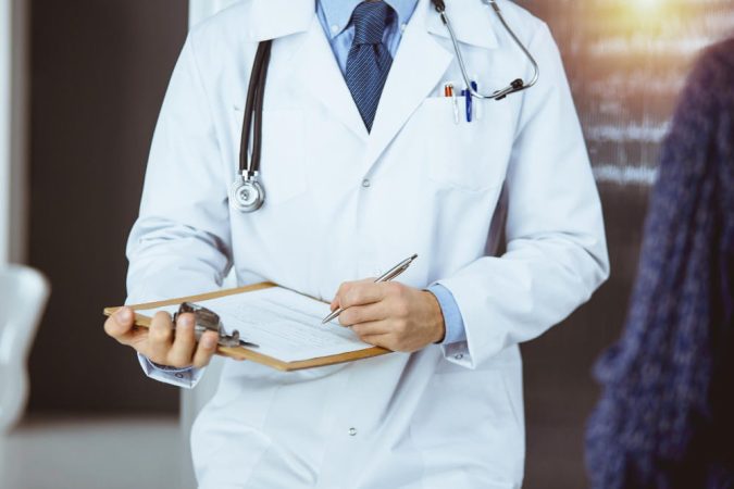 Gros plan d'un médecin de garde rédigeant une prescription sur un porte-bloc médical