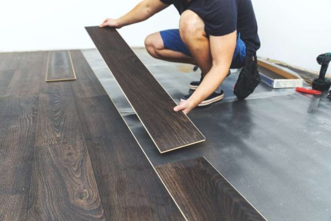Un artisan procède à la pose d'un revêtement de sol stratifié en bois sombre pour rénover une pièce.