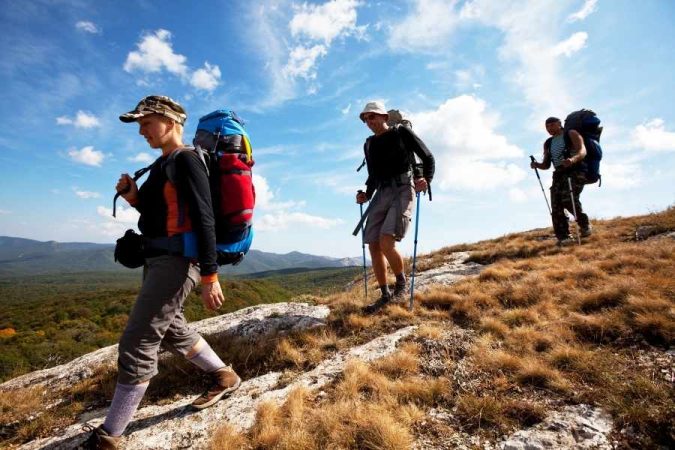 Trois amoureux de la randonnée marchent avec des sacs à dos sur une crête montagneuse ensoleillée.