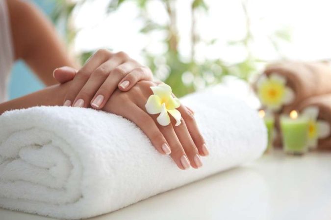 Des mains soignées avec une manucure naturelle reposent sur une serviette éponge blanche dans un spa.