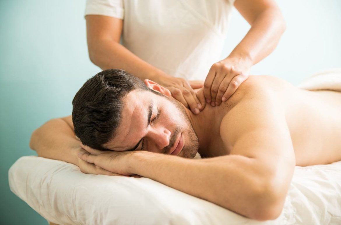 Homme allongé sur une table de soin recevant un massage thérapeutique réduction inflammation musculaire au niveau du dos et des épaules.